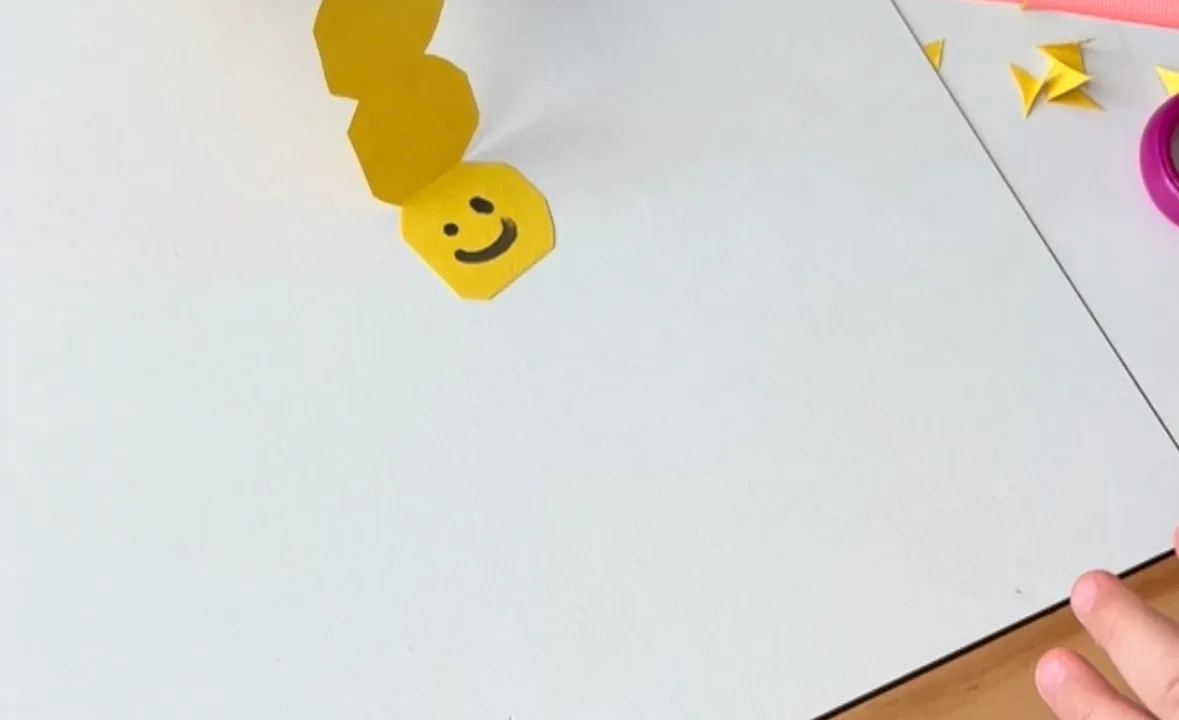 Toddler blowing through a straw to move a paper caterpillar across a hardwood floor