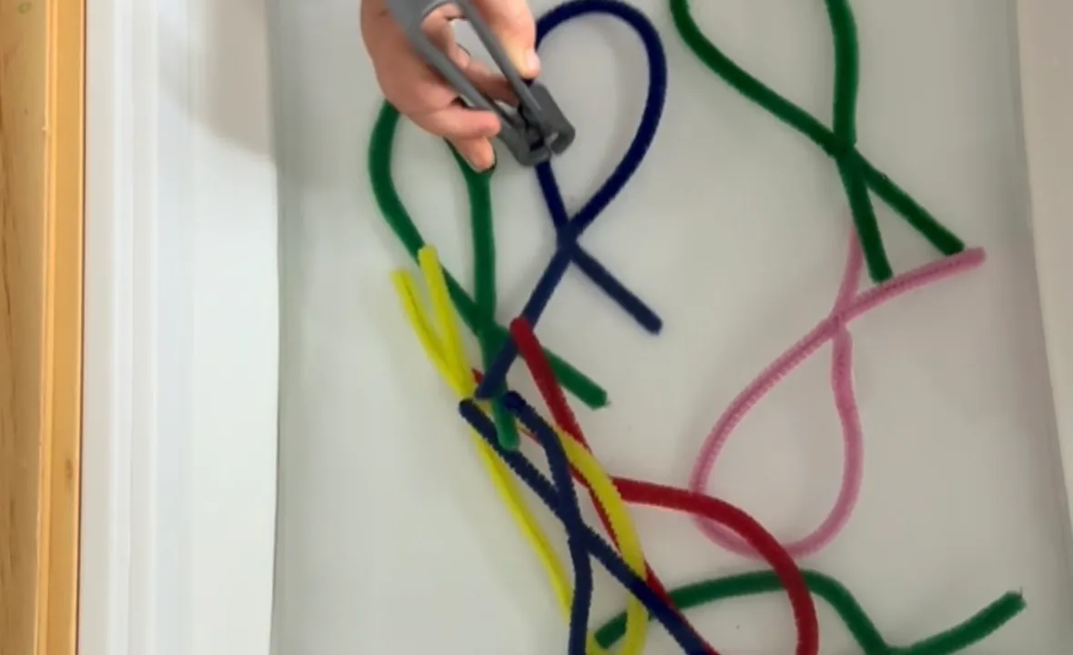 Toddler pulling colored pipe cleaners out of a clear bin filled with water