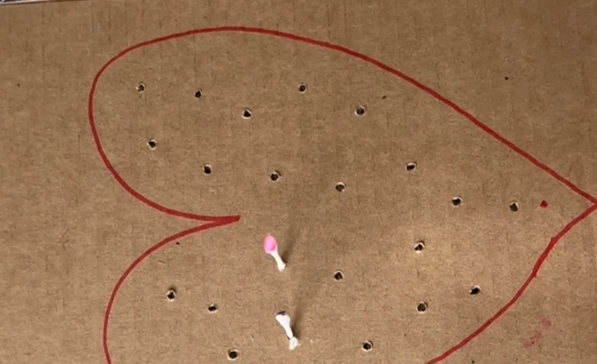 Toddler pushing Q-tips into a heart-shaped pattern of holes punched in cardboard