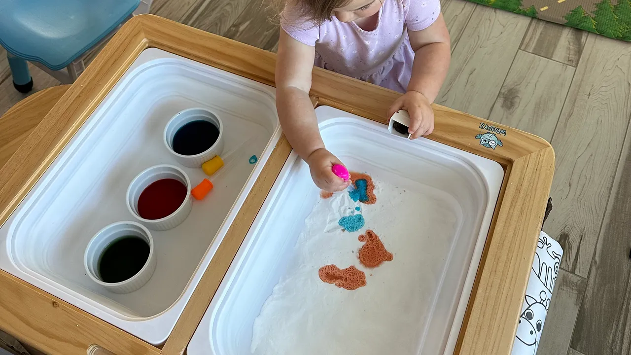 Toddler watching colored vinegar fizz and bubble in a tray of baking soda