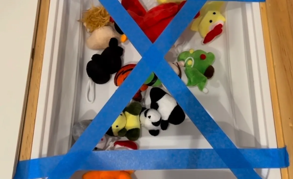 Toddler peeling painters tape off small plastic toys stuck to the bottom of a bin