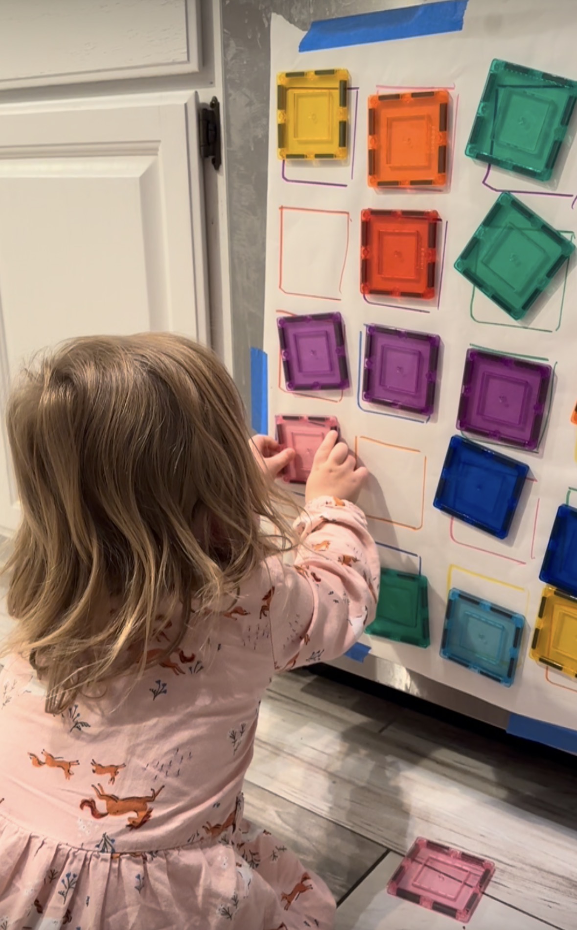 A toddler concentrating on an activity from the guide, hands engaged on a kitchen floor